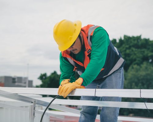 A construction worker with safety gear installing solar panels on a sunny day.
